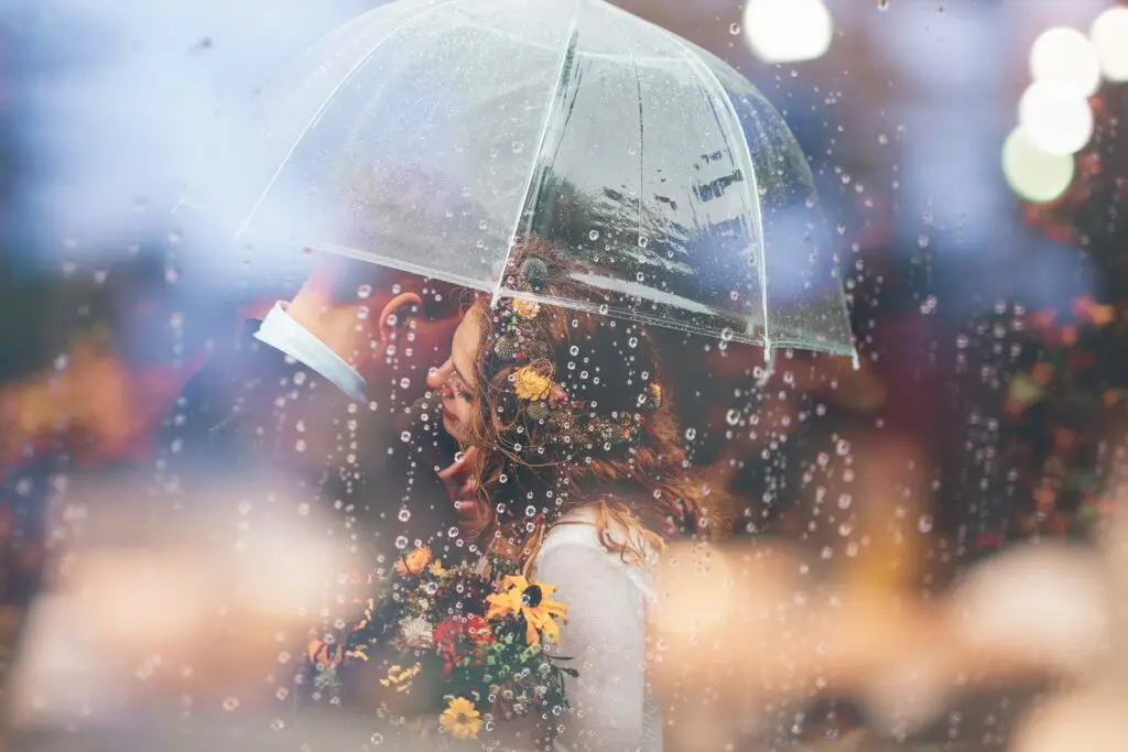 a bride and groom kiss in the rain under an umbrella